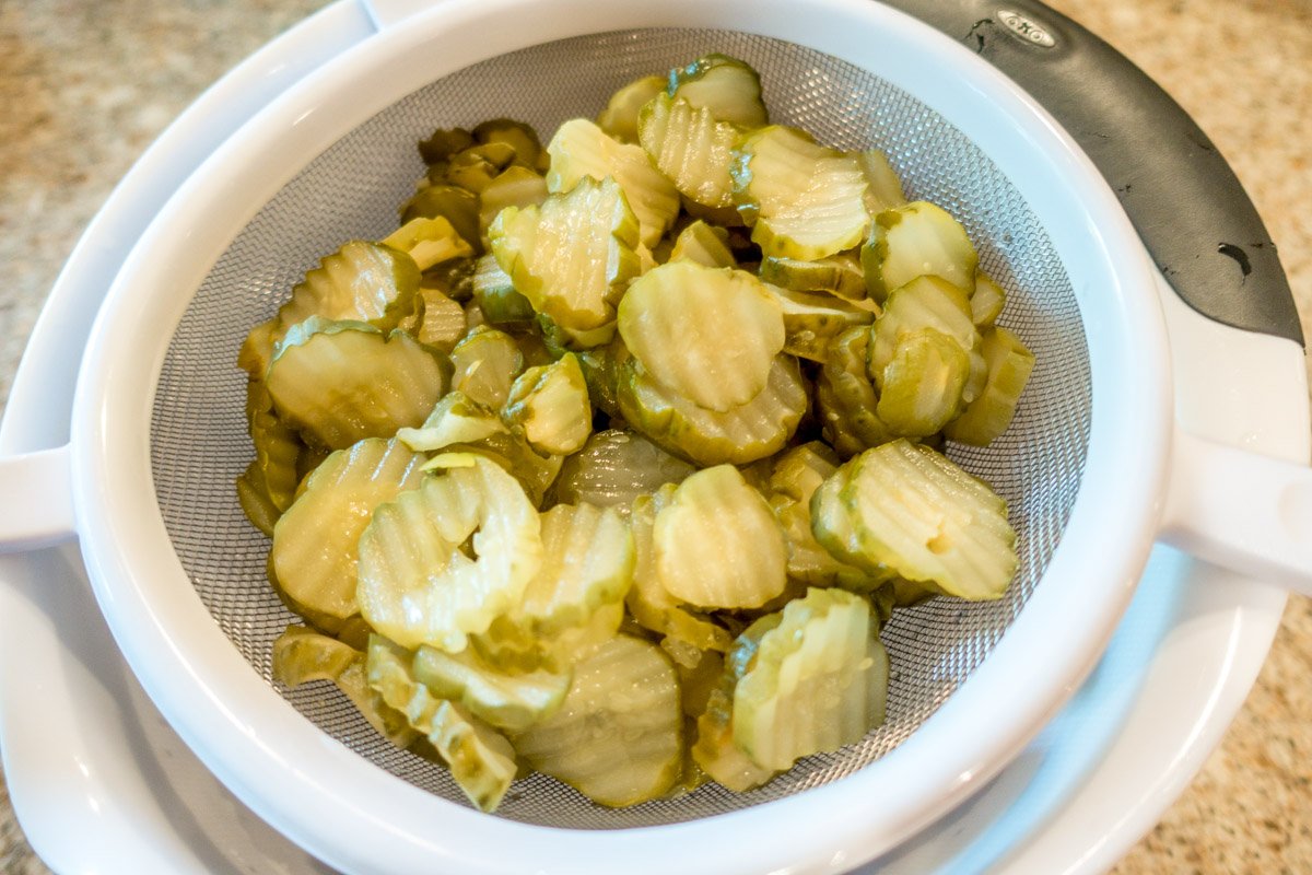 Pickle slices in a strainer to drain the brine over a white bowl