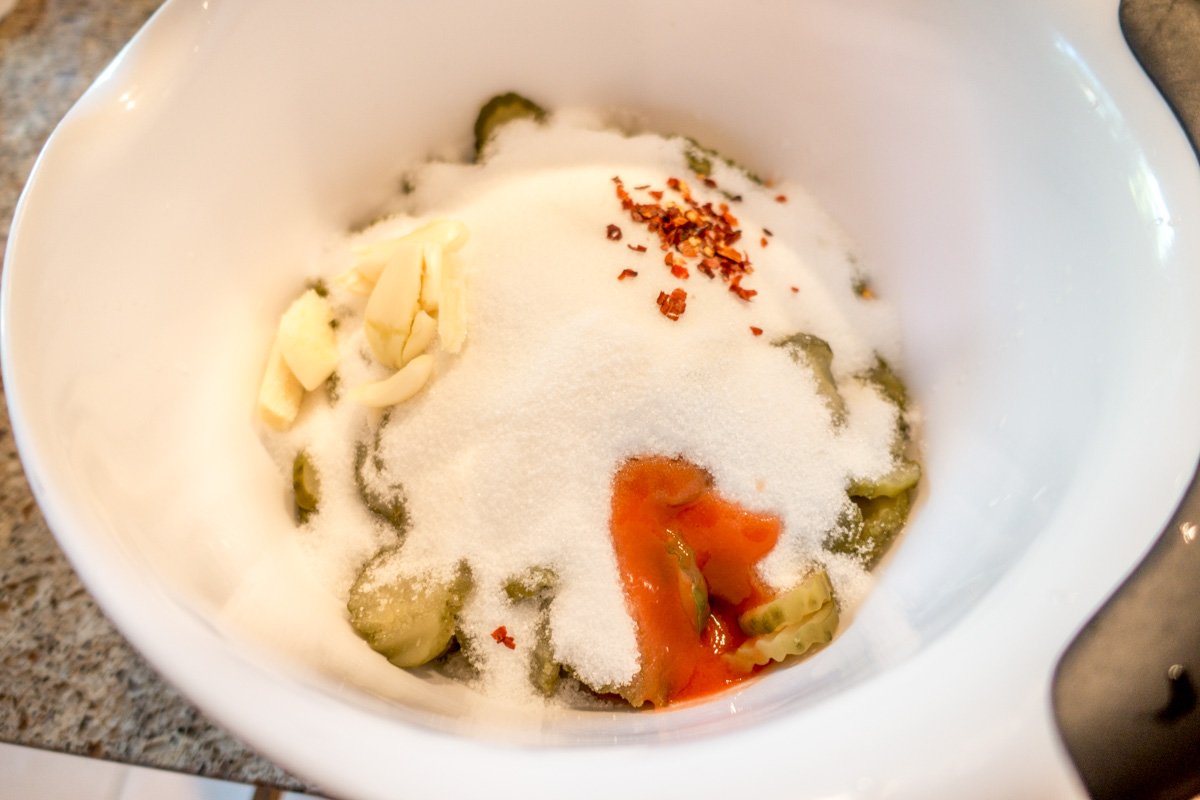 Sugar, garlic, hot sauce, and red pepper flakes in a bowl with pickle slices