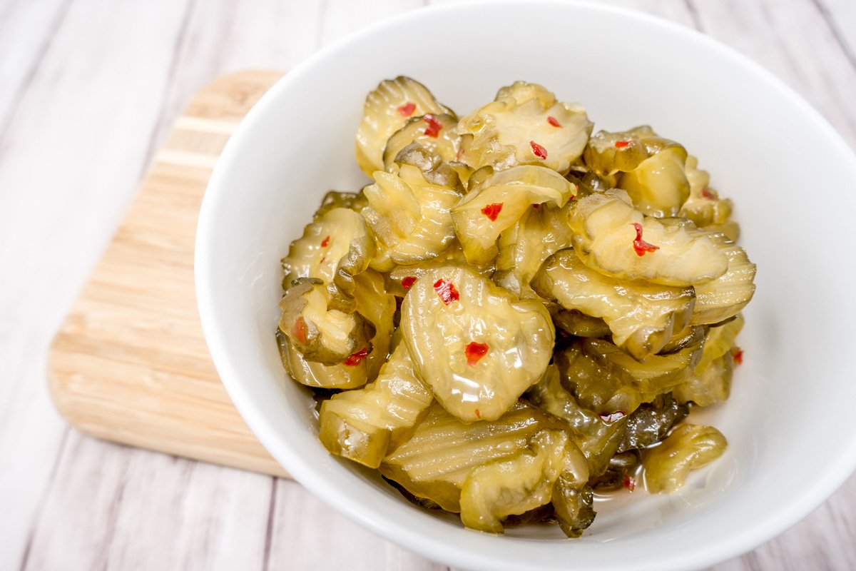 Fire and ice pickles (aka a Christmas pickles) in a white bowl on a wooden cutting board