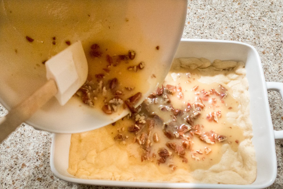 Pouring the pecan pie filling ingredients onto the pre-baked crust for bars