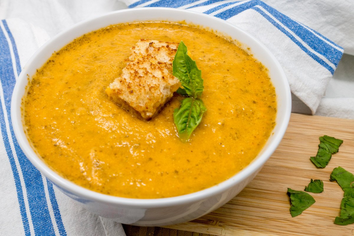 Easy roasted tomato soup with basil in a bowl with bite-sized grilled cheese sandwiches