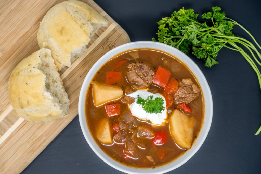 Finished German goulash in a bowl, topped with sour cream and served with crusty bread