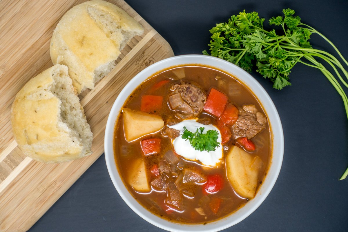 German goulash in a bowl with sour cream and served with crusty bread