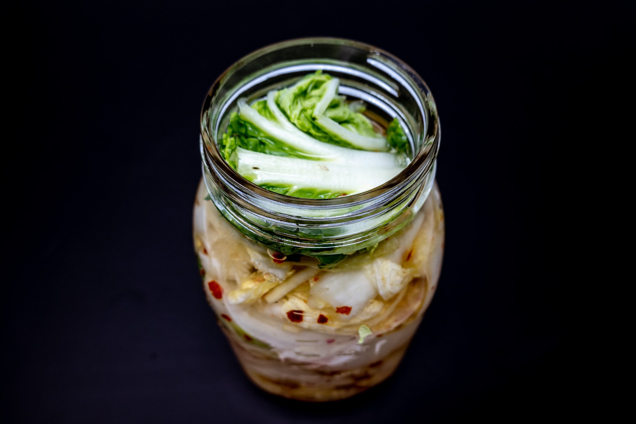 Baechu-kimchi fermenting in a jar with a cabbage leaf on top