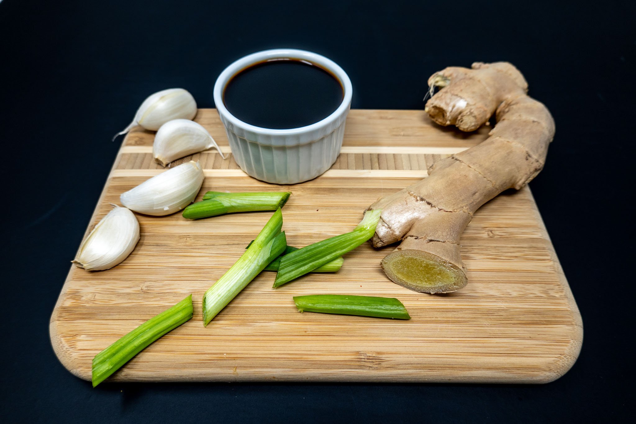 Garlic cloves, scallions, ginger, and soy sauce on cutting board