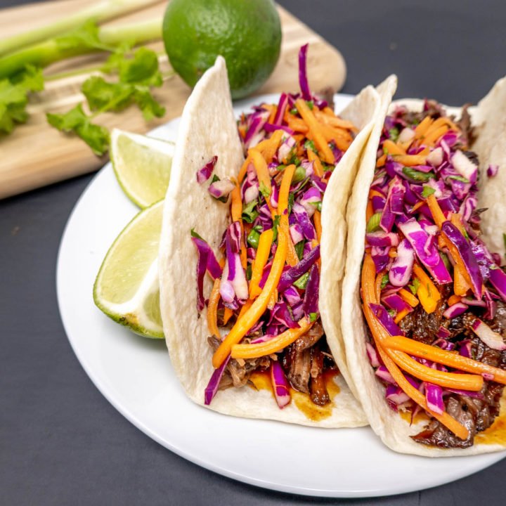 Tacos on a plate with limes and scallions