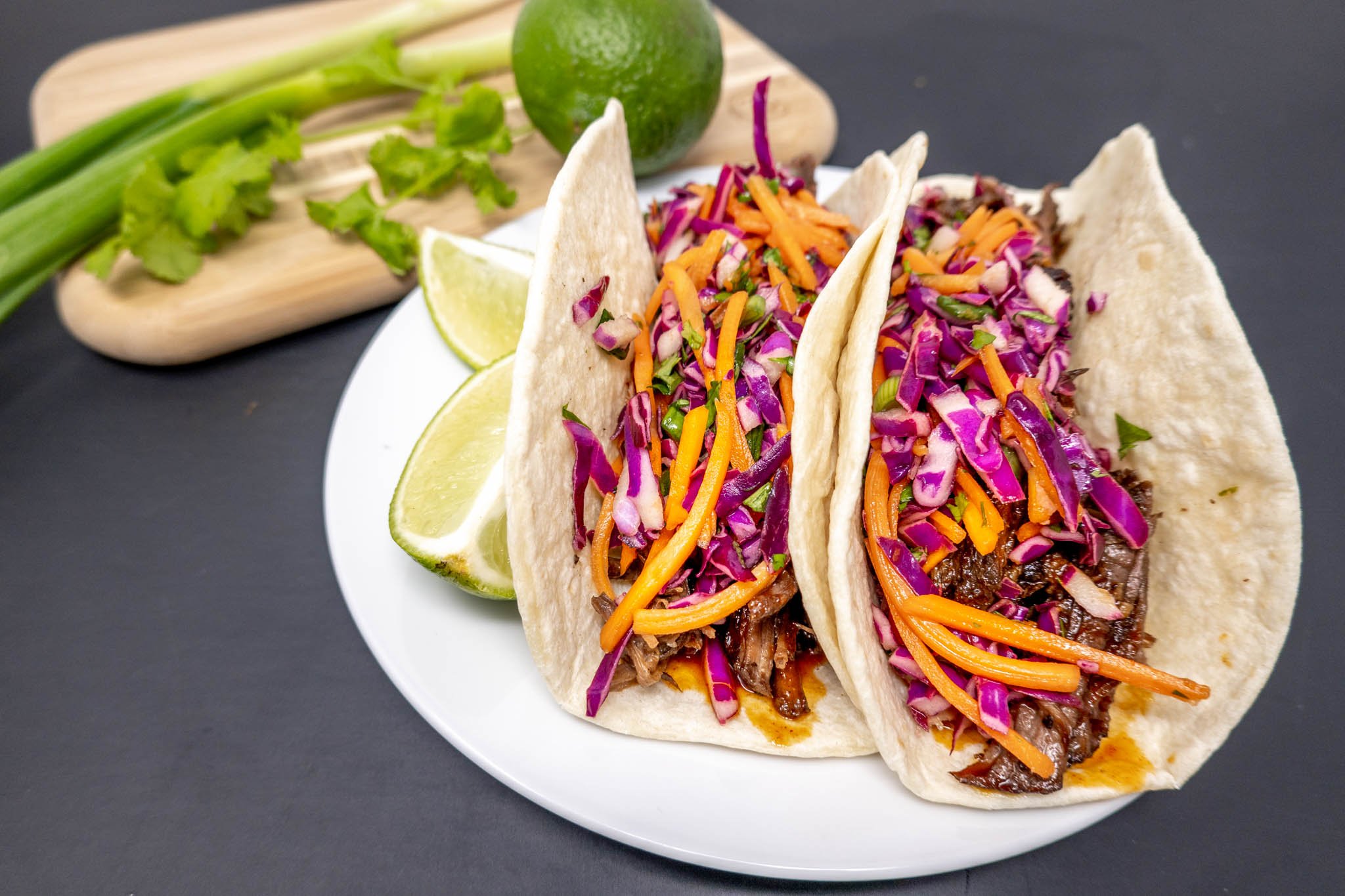 Tacos on a plate with limes and scallions