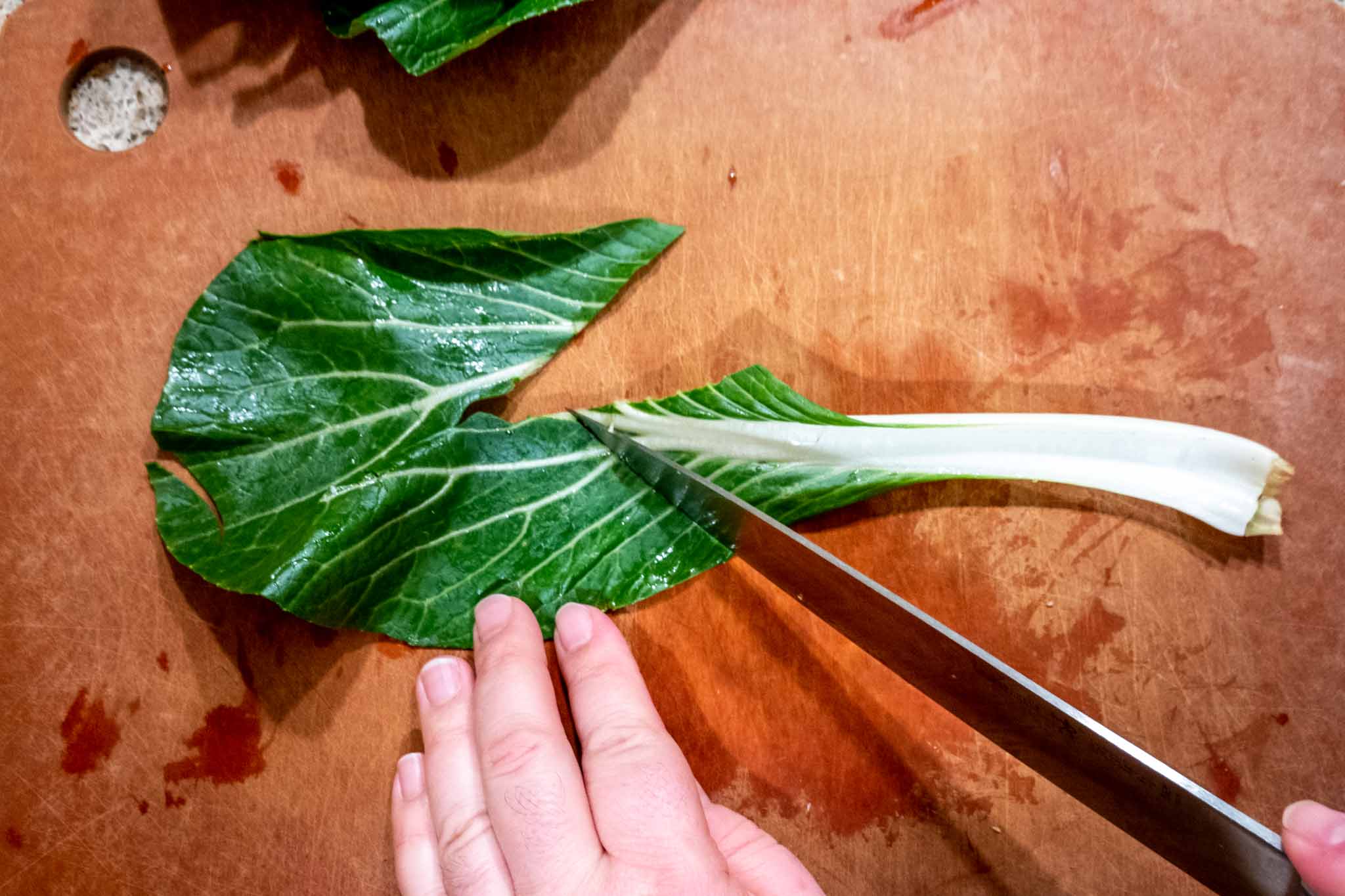 Person removing  bok choy stem from leaf with a knife