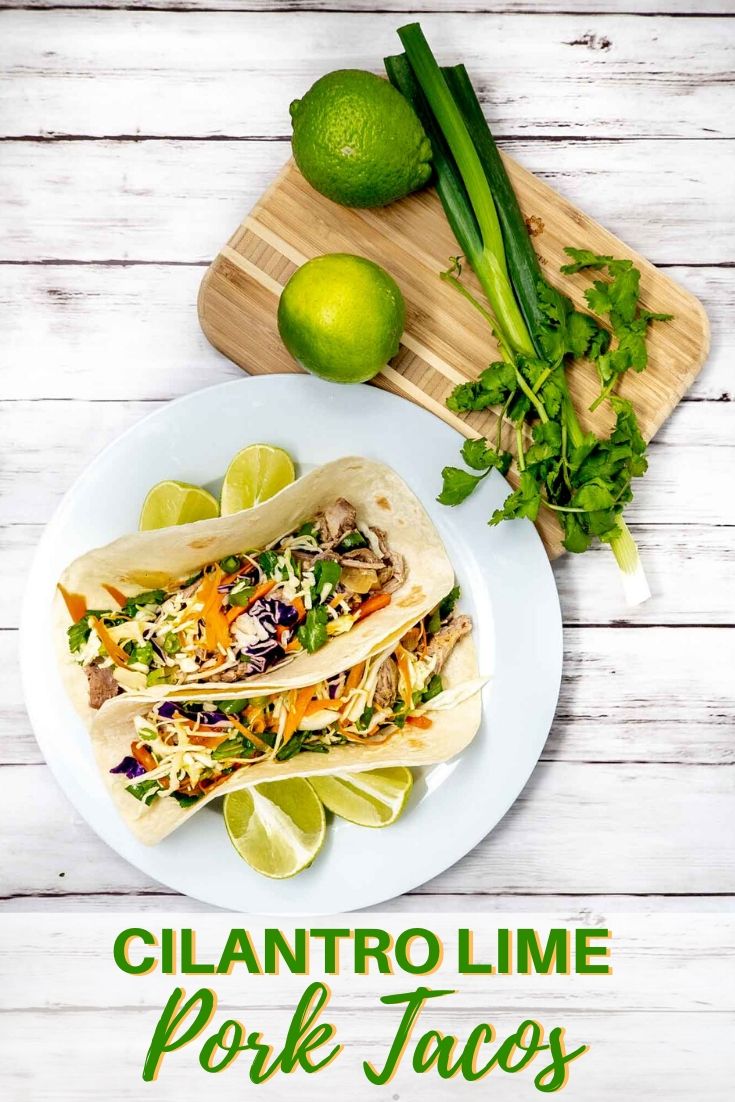 Overhead view of tacos on a plate alongside limes, scallions, and cilantro