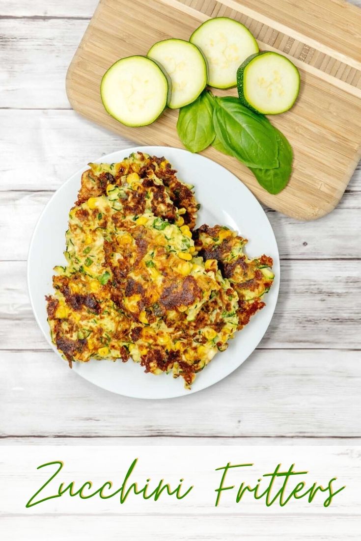 Zucchini corn fritters beside zucchini slices and basil leaves