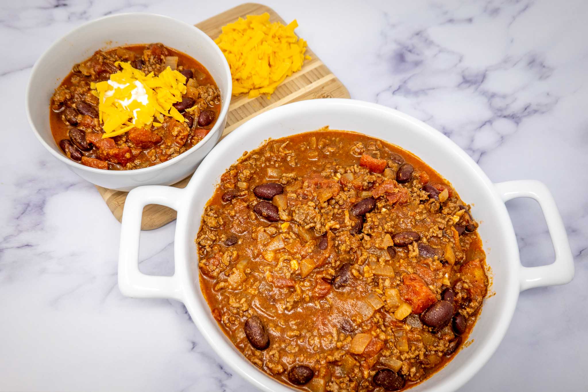 Dish and bowl of chili with shredded cheddar cheese