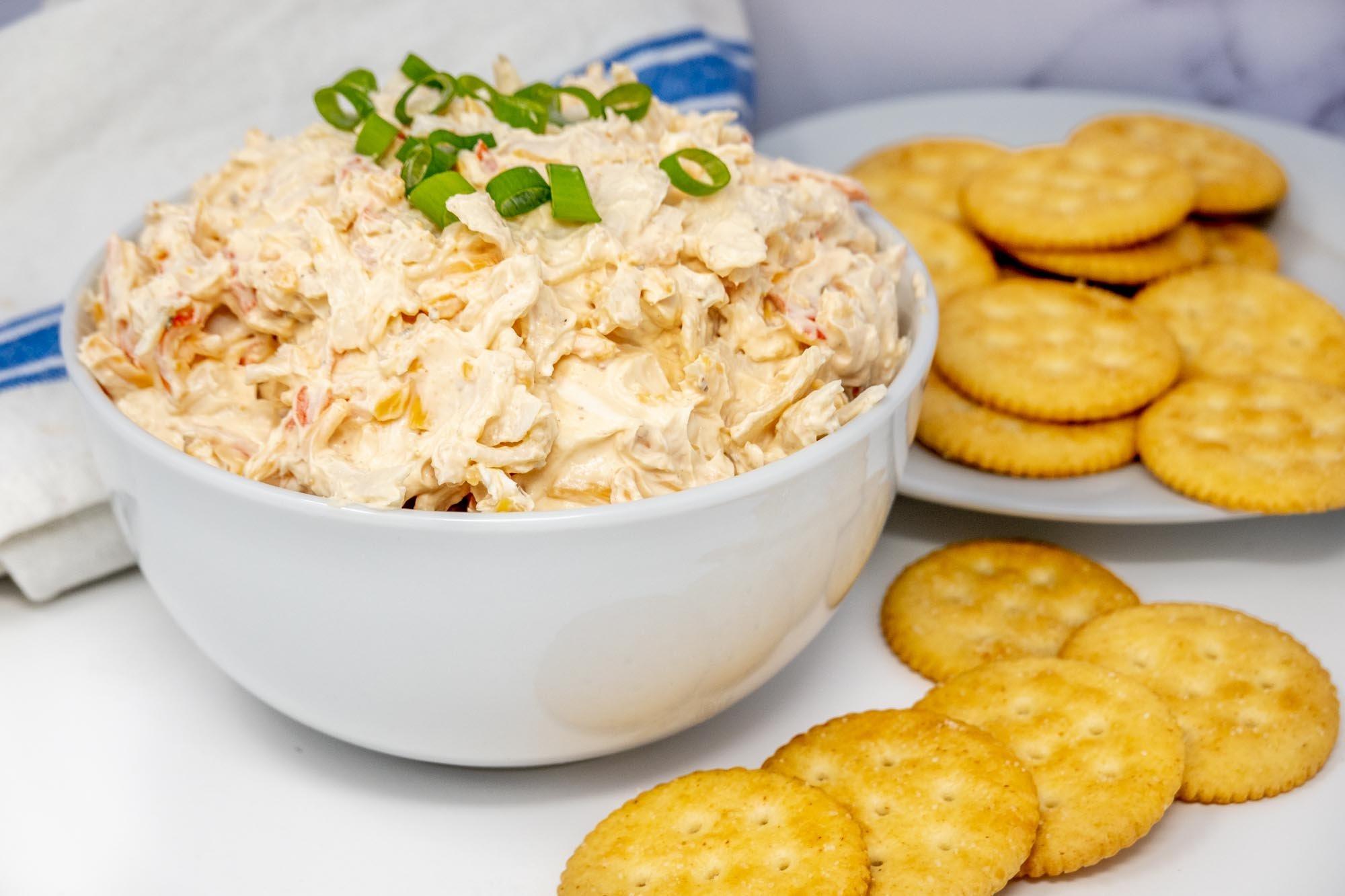 Bowl of crab dip topped with scallions beside a pile of Ritz crackers