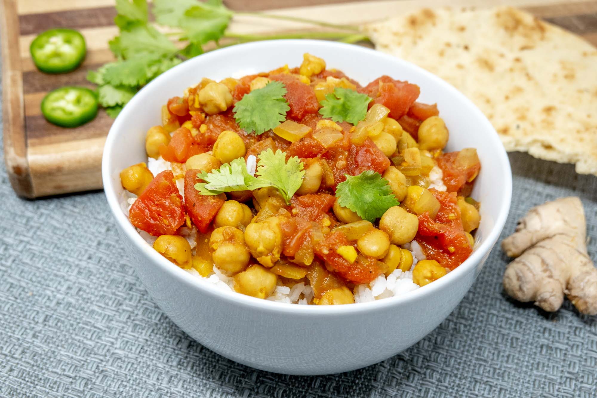 Bowl of rice topped with chickpea and tomato mixture beside ginger and jalapeno slices