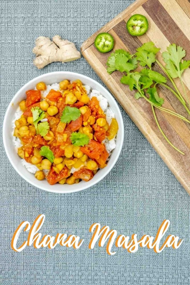 Chana masala over rice in a bowl next to a piece of ginger, cilantro, and slices of jalapeno