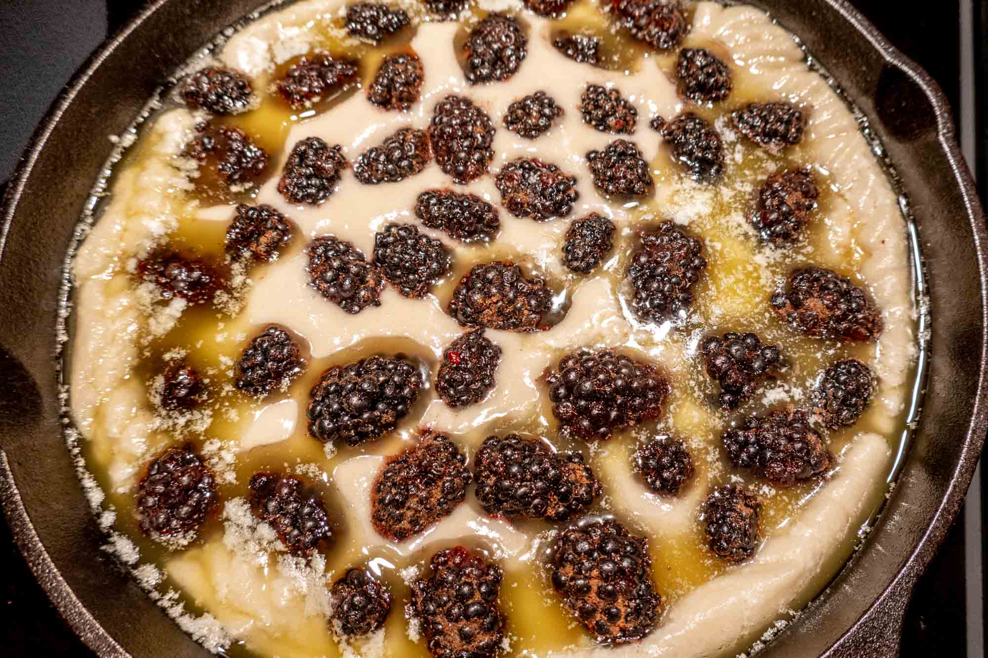 Batter topped with blackberries and melted butter in a cast iron skillet