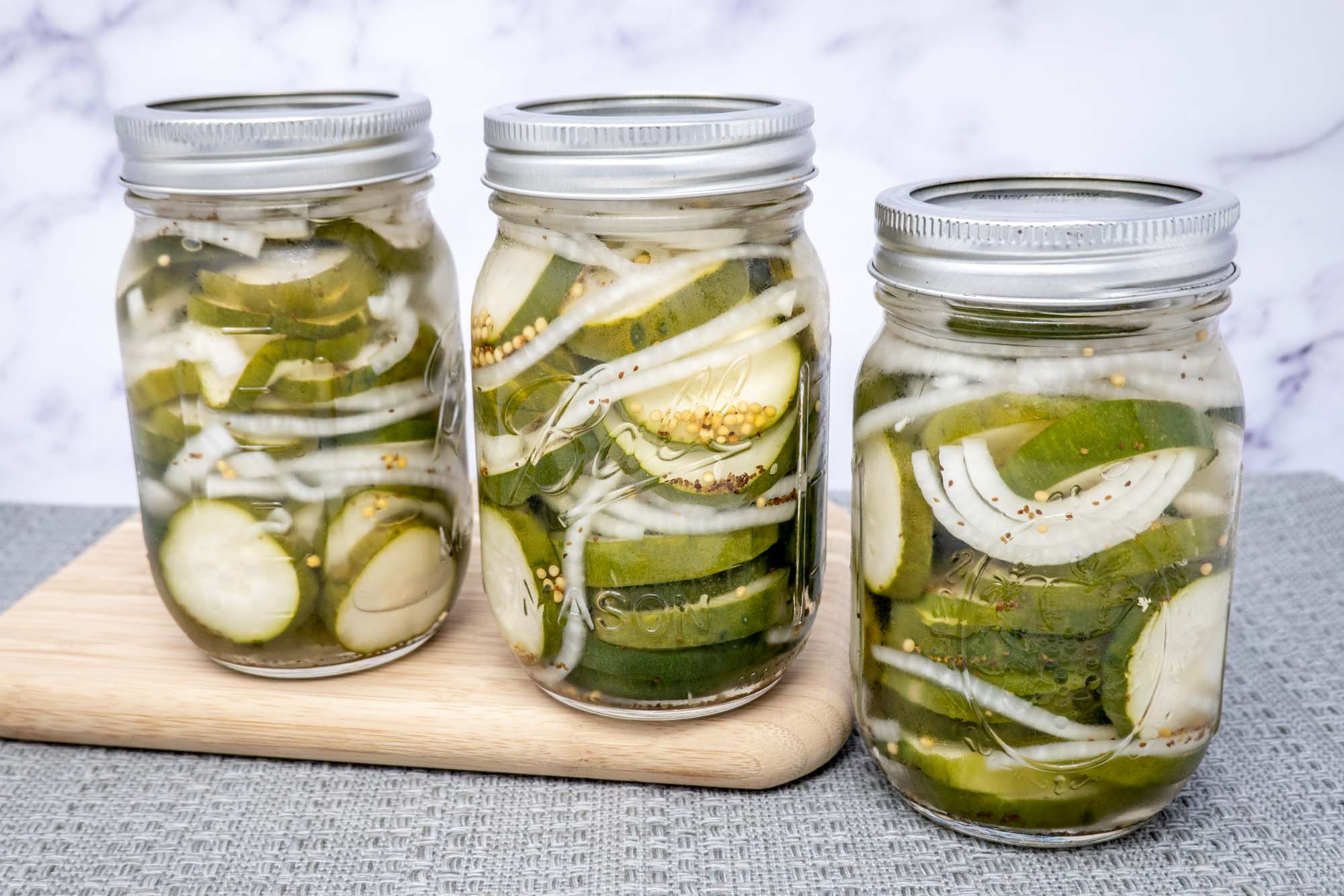 Three jars of pickled cucumbers and onions two of which are sitting on a cutting board