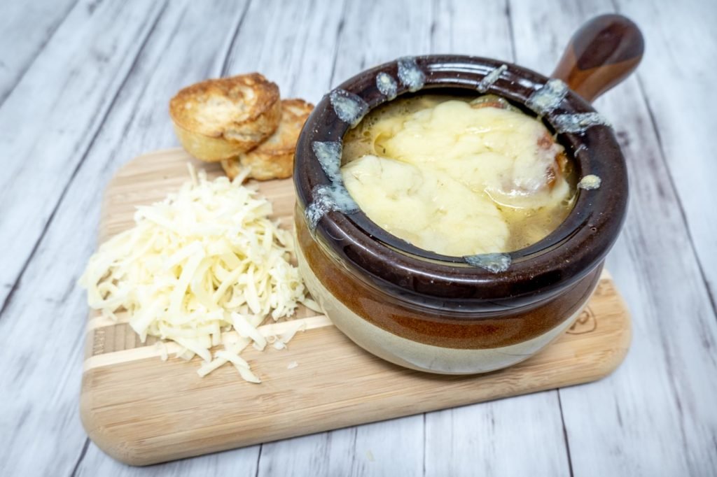 Crock of soup covered with cheese beside a pile of shredded cheese and croutons